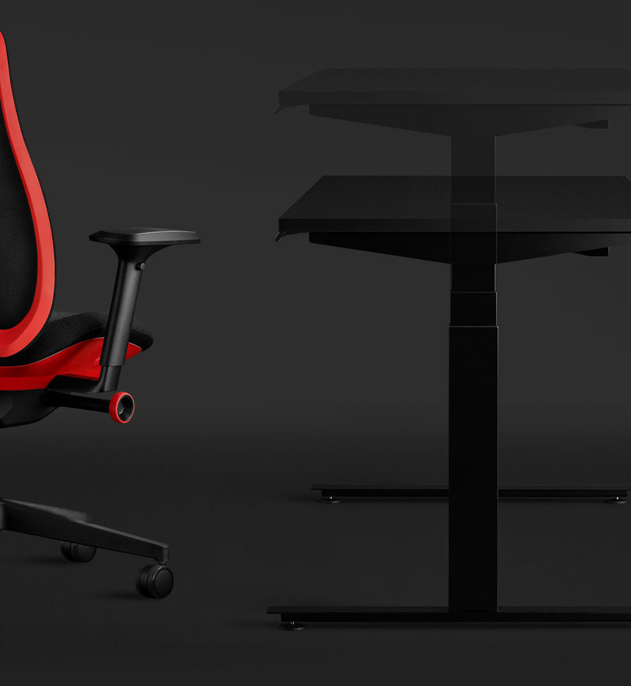 Seitenansicht eines schwarzen Nevi Gaming-Schreibtisches und eines roten Vantum Gaming-Stuhls von Herman Miller, wobei das Sitz-Steh-Element des Schreibtisches hervorgehoben wird.