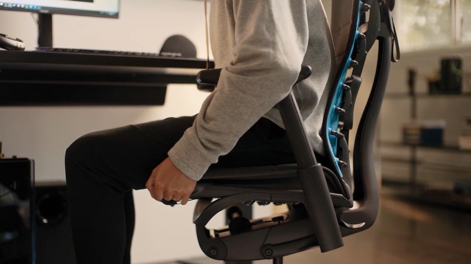 Ein Video von einer Person, die in einem schwarz-blauen Embody Gaming-Stuhl von Herman Miller sitzt und neben den Stuhl greift, um die Sitztiefe einzustellen.