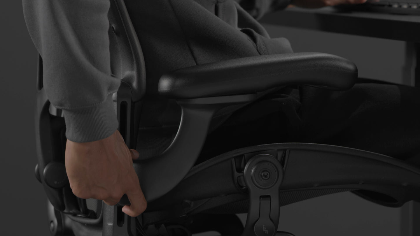 Ein Video von einer Person, die in einem schwarzen Aeron-Gaming-Stuhl von Herman Miller sitzt und neben den Stuhl greift, um die Armlehnen zu verstellen.