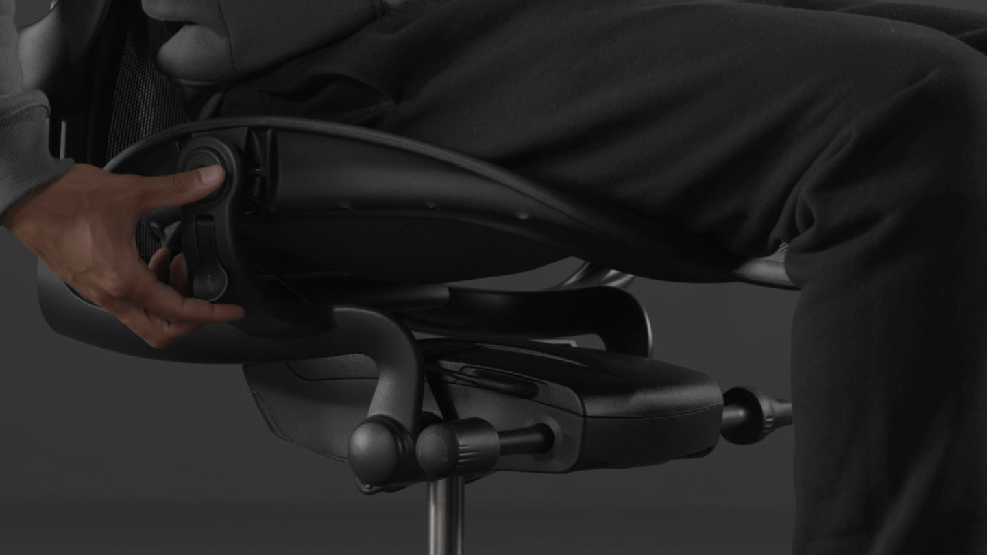 Ein Video von einer Person, die in einem schwarzen Aeron-Gaming-Stuhl von Herman Miller sitzt und neben den Stuhl greift, um die Sitzhöhe einzustellen.