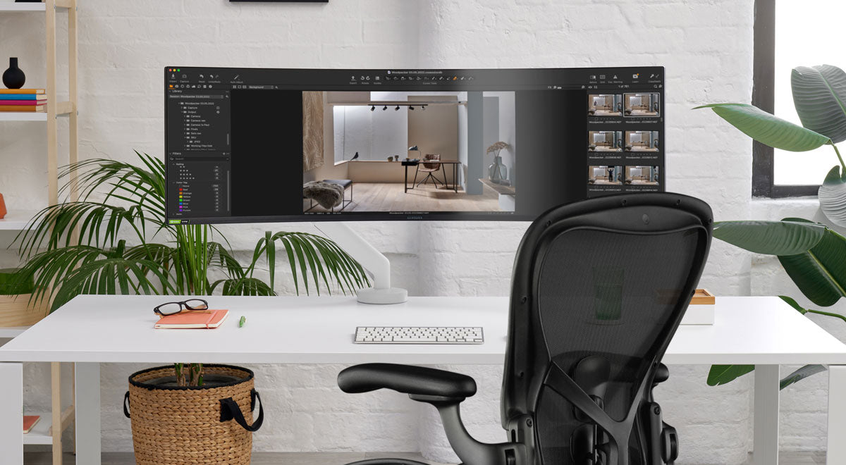 Vorderansicht eines weißen Flo X-Monitorarms von CBS, der an einem weißen Schreibtisch vor einem schwarzen Aeron-Bürostuhl von Herman Miller angebracht ist.