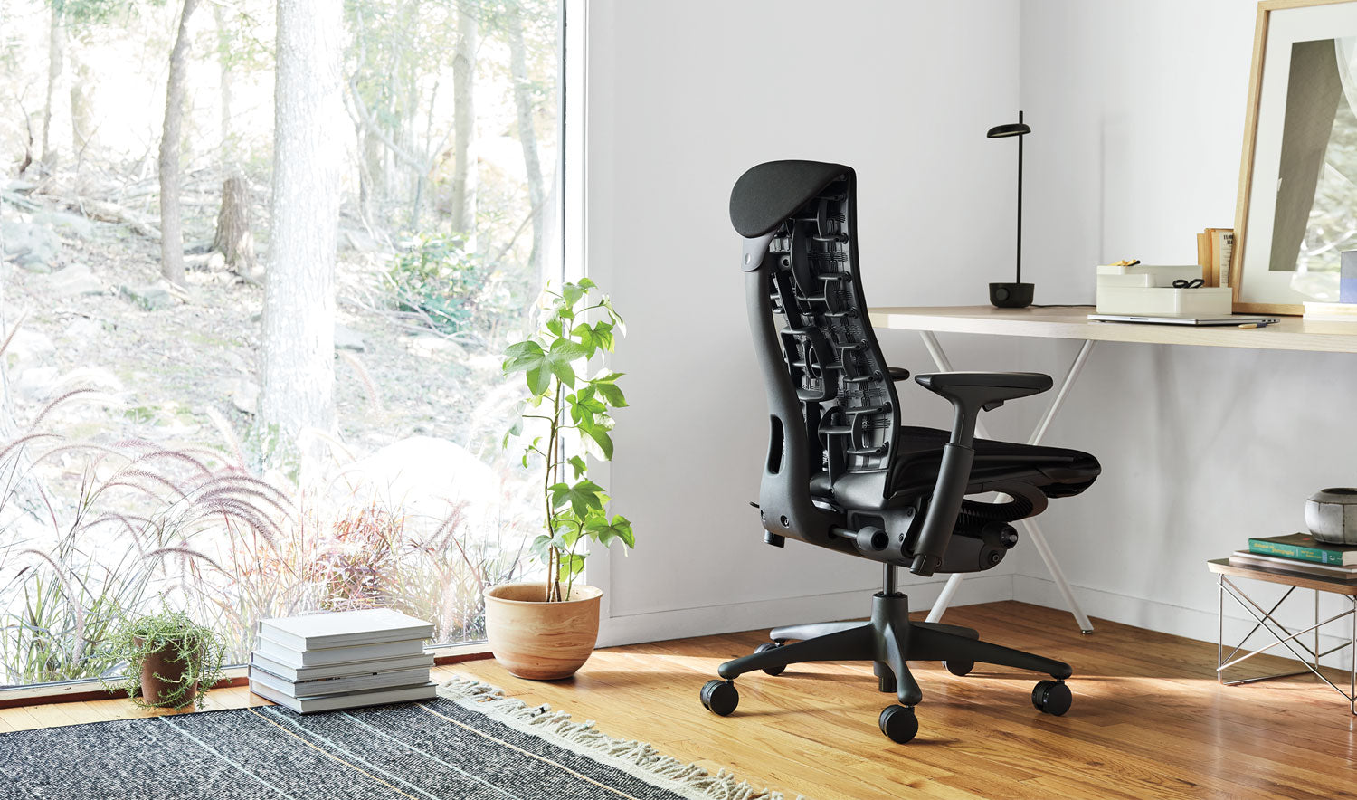 Ein schwarzer Embody-Bürostuhl von Herman Miller, der in einem Innenraum steht. Der Raum enthält Elemente wie Möbel, Bodenbeläge und dekorative Gegenstände wie einen Blumentopf und eine Vase.