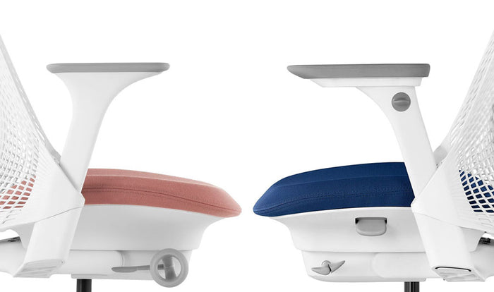 Seitenansicht von zwei Herman Miller Sayl Bürostühlen, die sich gegenüberstehen. Der linke Stuhl zeigt die feste Armlehne, der rechte Stuhl die voll verstellbare Armlehne.