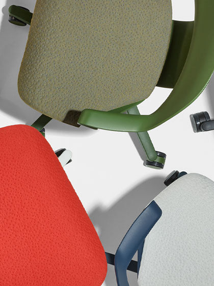 Draufsicht auf drei Herman Miller Zeph-Bürostühle in Grün, Rot und Blau, die die Textur der Sitzpolster zeigen.