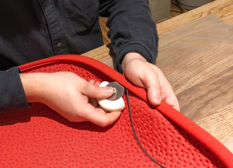 Eine Person, die ein rotes Sitzpolster aus Stoff für einen Herman Miller Zeph-Bürostuhl herstellt.
