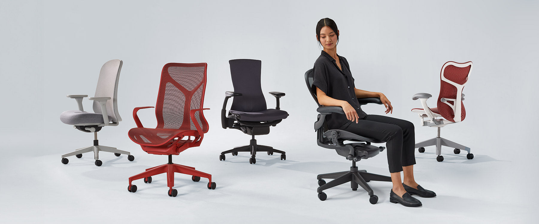 Foto von Herman Miller-Stühlen, die aufgereiht sind, darunter Verus mineral white & grey, Cosm mid back in canyon red, Embody black, Aeron graphite with lady sat in und Mirra 2 in cordovan red