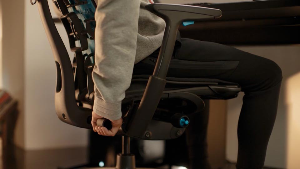 Ein Video von einer Person, die in einem schwarz-blauen Embody Gaming-Stuhl von Herman Miller sitzt und hinter den Stuhl greift, um die Rückenlehne zu verstellen.
