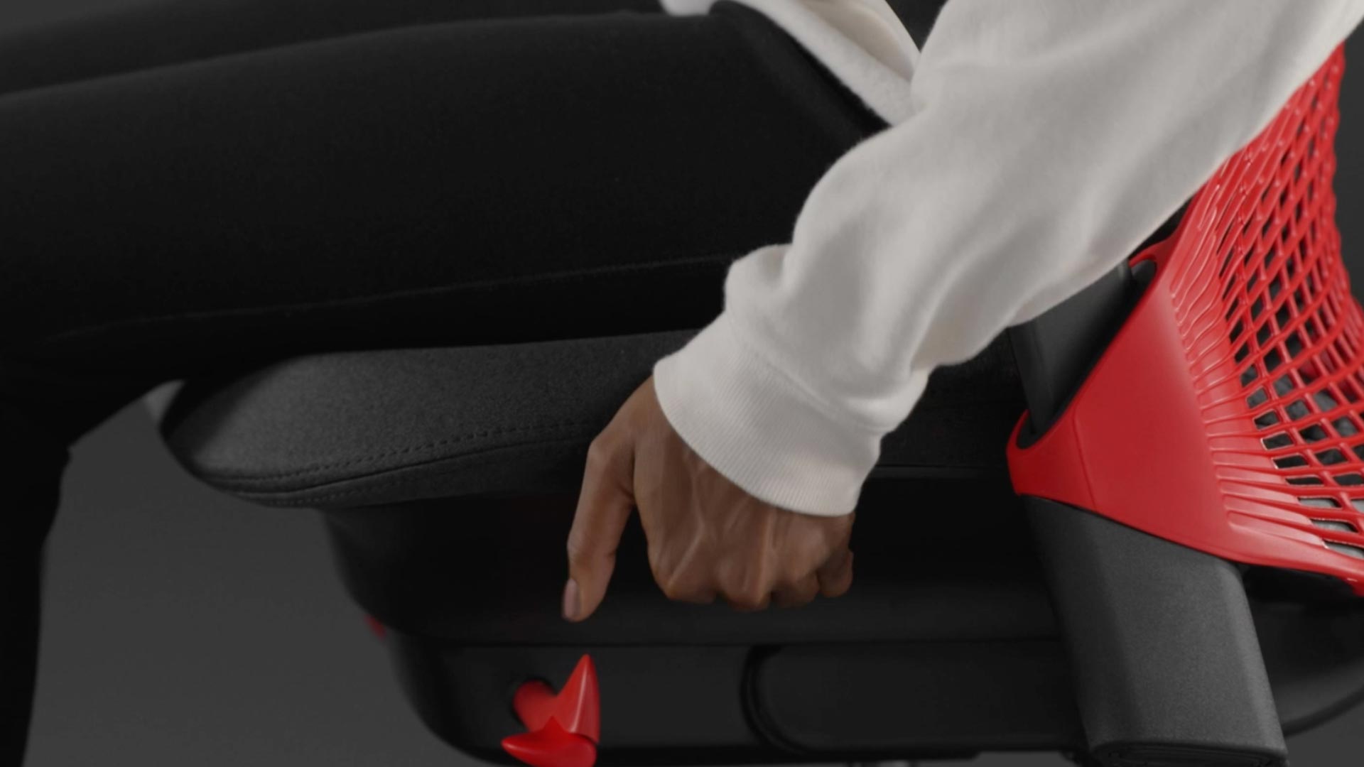 Ein Video von einer Person, die in einem rot-schwarzen Sayl-Gaming-Stuhl von Herman Miller sitzt und neben den Stuhl greift, um die Sitztiefe einzustellen.
