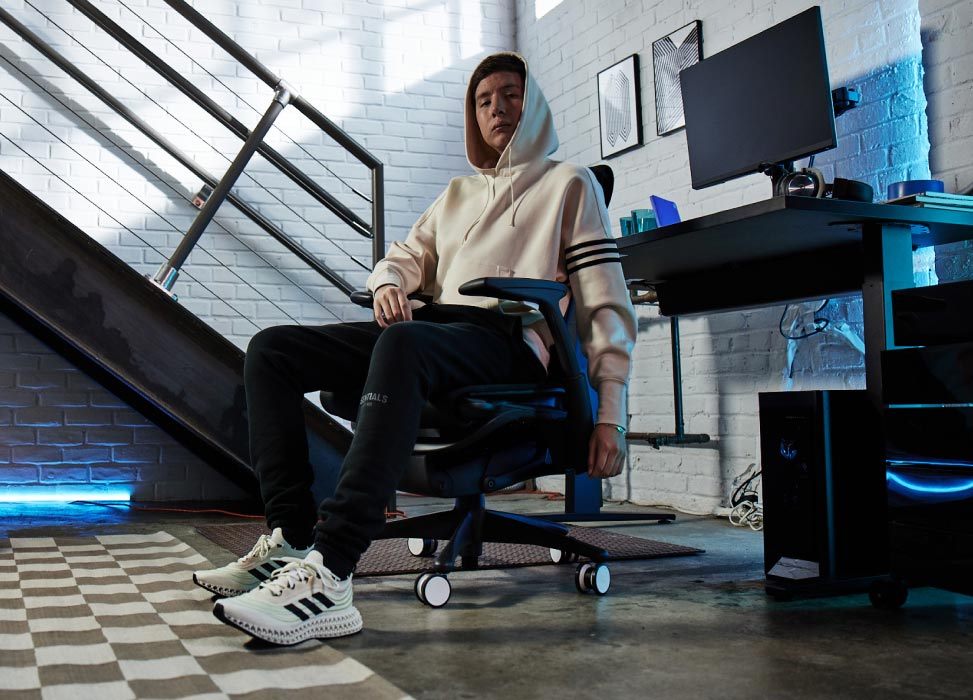 Foto von Jelty vom G2 Esports-Team, der auf dem G2 Embody-Stuhl sitzt, mit dem Gaming-Setup im Hintergrund, darunter ein Nevi-Gaming-Tisch in Schwarz mit Ollin-Monitoren