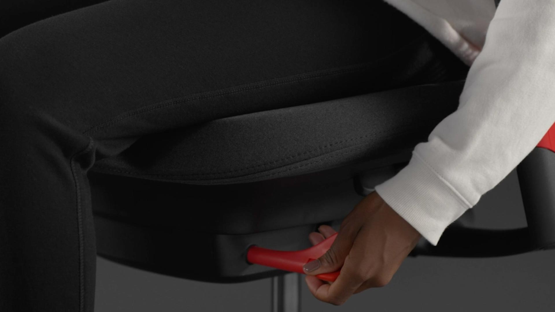 Ein Video von einer Person, die in einem rot-schwarzen Sayl-Gaming-Stuhl von Herman Miller sitzt und neben den Stuhl greift, um die Vorwärtsneigung einzustellen.