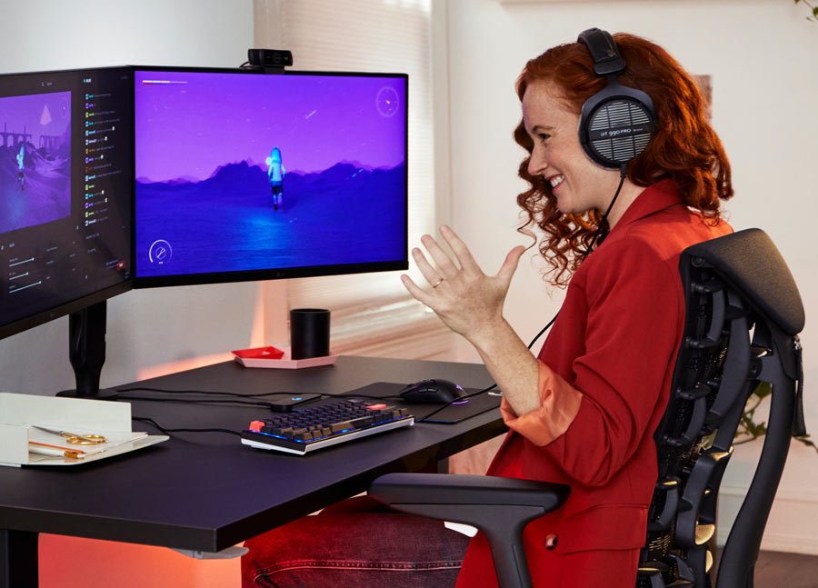 Foto von Dr. Lindsey Migliore, die lächelnd ein Computerspiel auf dem Embody-Gaming-Stuhl in Cyan mit dem Nevi-Gaming-Tisch in Schwarz spielt