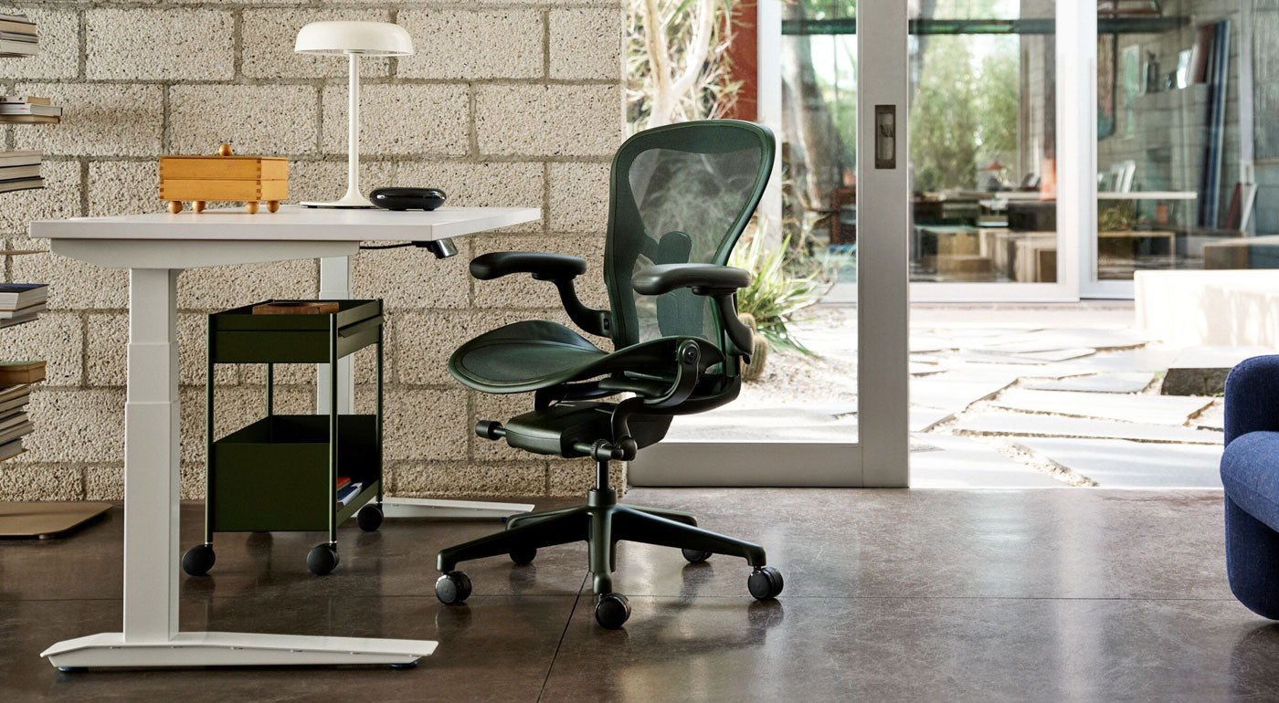 Ein Herman Miller Aeron-Schreibtischstuhl in Jasper (Grün) als Teil eines hellen Heimbüros mit einem weißen Jarvis-Steh-Sitz-Schreibtisch und einem olivgrünen OE1-Rollwagen.