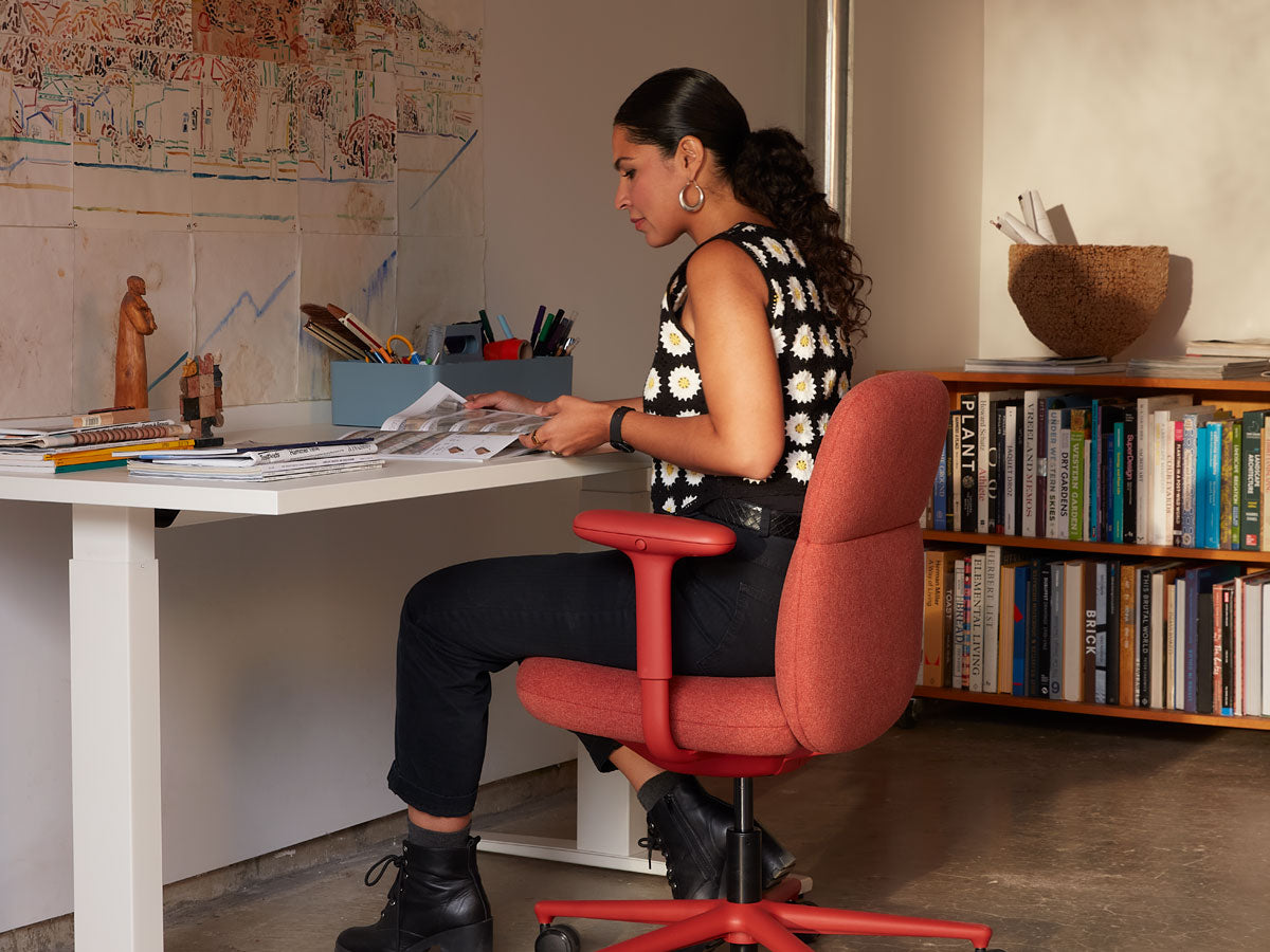 Anooshey Rahim saß an einem Nevi-Steh-Sitz-Schreibtisch und arbeitete auf einem Asari-Bürostuhl in Canyonrot.
