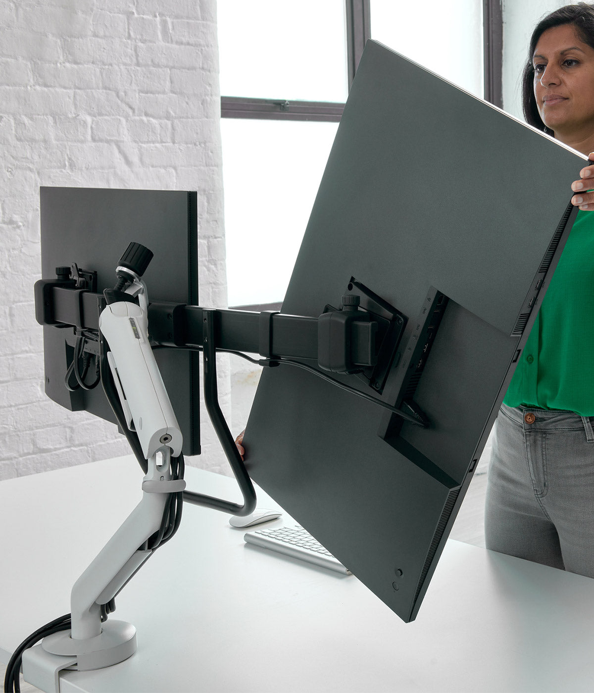 Ein großformatiger CBS Flo X-Monitorarm, der zwei Bildschirme trägt, während ein Benutzer die Ausrichtung anpasst.
