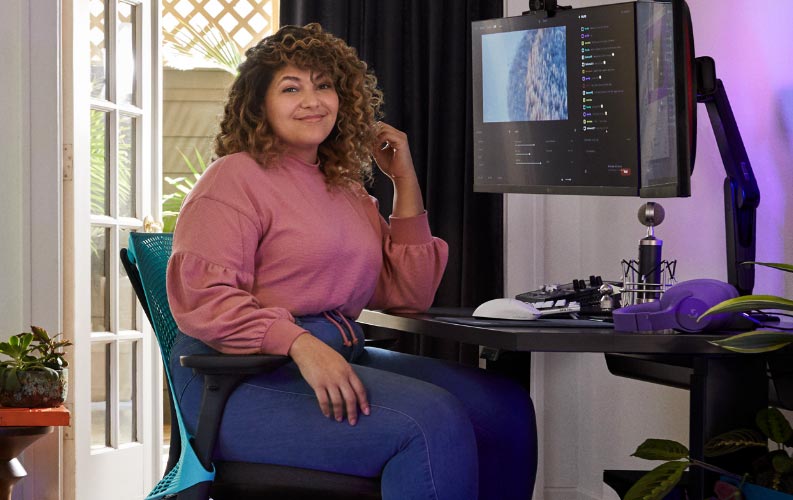 Profi-Streamer und Synchronsprecher Friskk saß auf einem Herman Miller Sayl Gaming-Stuhl in Ocean Deep Blue und Schwarz an einem schwarzen Nevi Gaming-Sitz-Stehpult mit Monitor auf einem Oliin-Monitorarm.