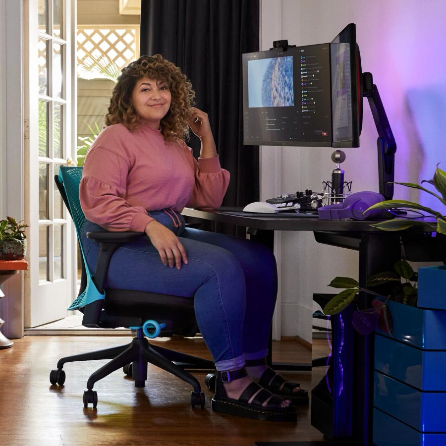 Pro-Streamer und Synchronsprecher Friskk saß auf einem Herman Miller Sayl-Gaming-Stuhl in Ozeanblau und Schwarz an einem schwarzen Nevi-Sitz-Steh-Gaming-Schreibtisch mit Monitor auf einem Oliin-Monitorarm.