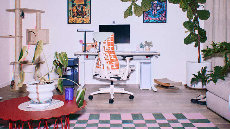 Ein weiß-orangefarbener Herman Miller Embody Gaming-Stuhl mit grauer Polsterung in einer hell beleuchteten PC-Gaming-Ecke im Wohnzimmer.