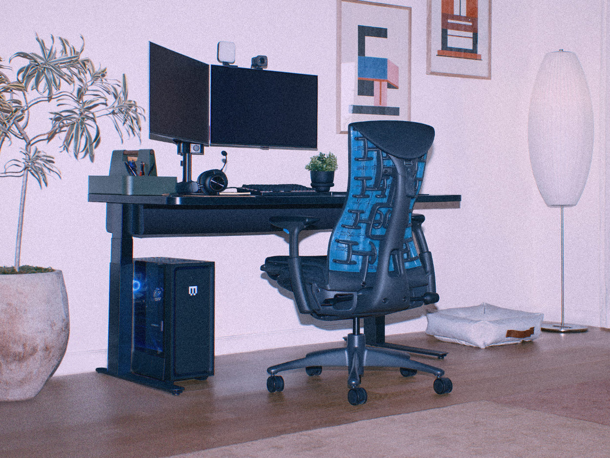 Eine PC-Gaming-Ausstattung mit zwei Monitoren auf einem CBS Lima-Monitorarm, befestigt an einem Nevi-Steh-Sitz-Schreibtisch mit einem Herman Miller Embody Gaming Chair in Schwarz und Blau.