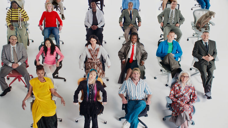 Eine große, vielfältige Gruppe von Menschen saß auf einer Auswahl ergonomischer Bürostühle von Herman Miller in einer weißen Studioumgebung.