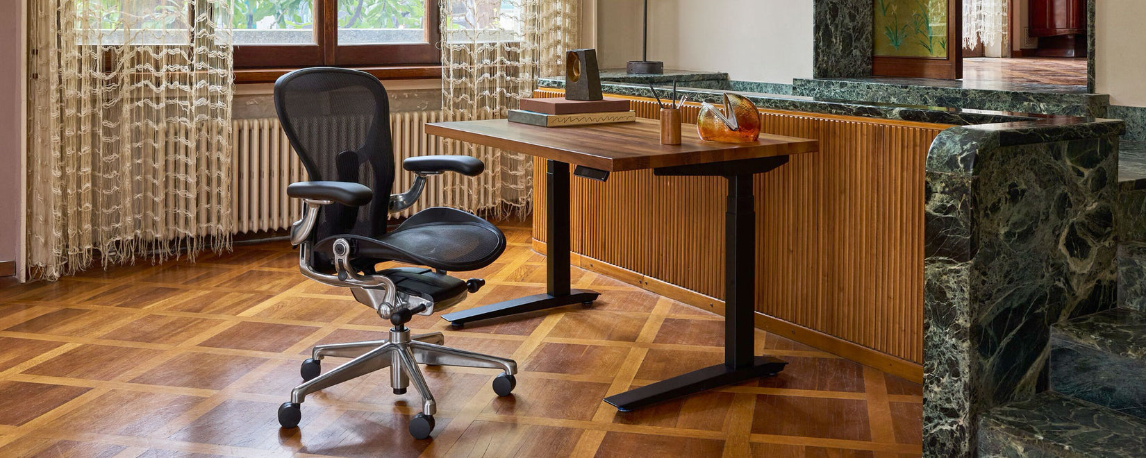 Ein Herman Miller Aeron in Onyxschwarz und poliertem Aluminium neben einem Jarvis Sitz-Steh-Schreibtisch mit Nussbaum-Platte in einem mediterranen Home-Office mit Holzvertäfelung und schwarzem Smaragdmarmor.