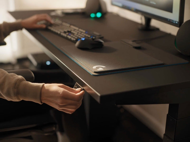 Ein Video von einer Person, die an einem schwarzen Nevi-Gaming-Schreibtisch von Herman Miller sitzt und einen Knopf drückt, um die Tischplatte abzusenken.