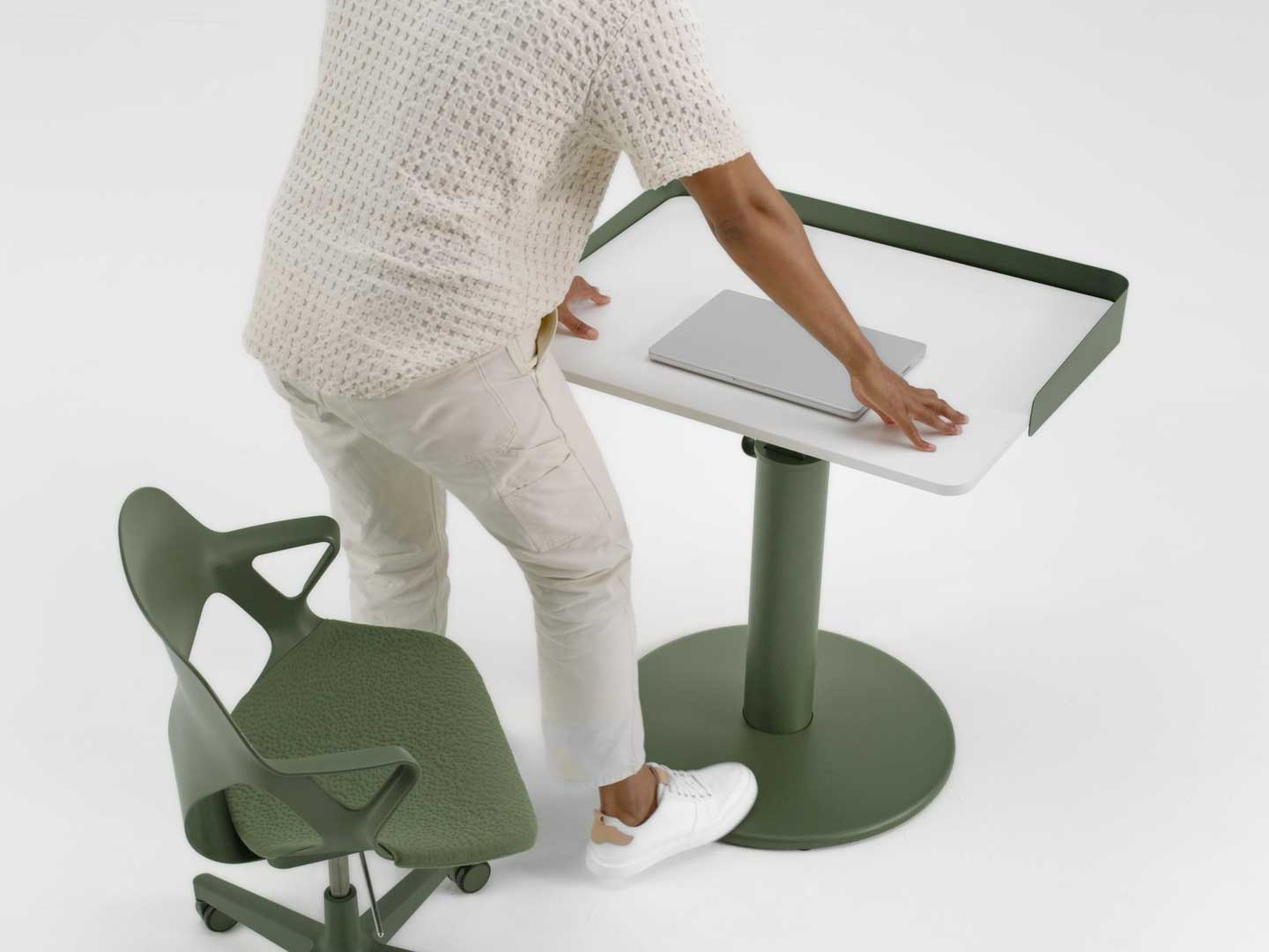 Ein Video, in dem ein Mann von einem grünen Zeph-Stuhl von Herman Miller aufsteht und mit dem Fuß die Höhe eines grün-weißen OE1-Stehpults von Herman Miller verstellt.