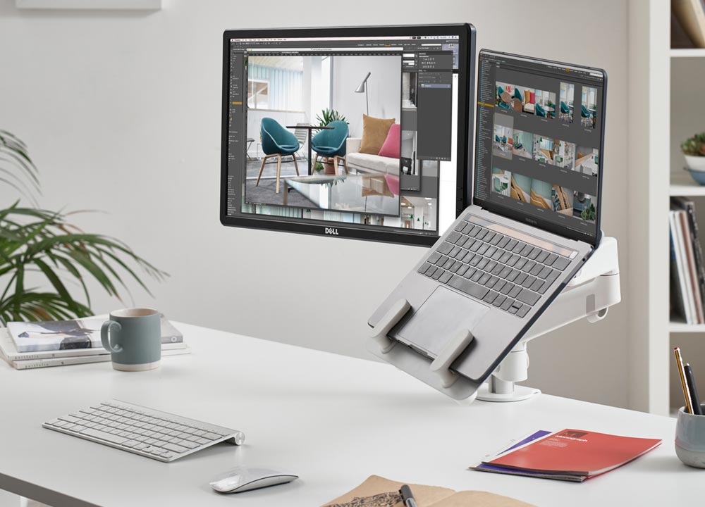 Ein weißer Lima-Doppelmonitorarm von CBS mit weißer Laptophalterung, der den Computerbildschirm und die Laptophalterung zeigt.