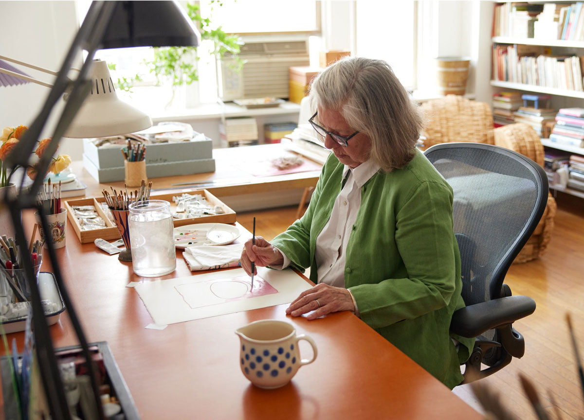 Frontansicht einer Illustratorin, Malerin und Autorin, die in einem Aerong-Bürostuhl in Graphit am Schreibtisch sitzt und malt