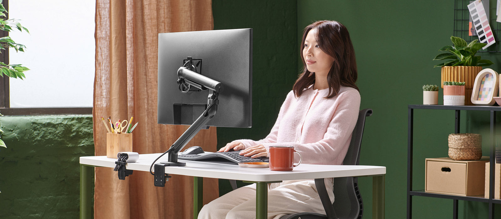 Eine Frau saß an einem Herman Miller OE1-Schreibtisch und arbeitete an einem Bildschirm, der von einem schwarzen Flo-Monitorarm gehalten wurde.