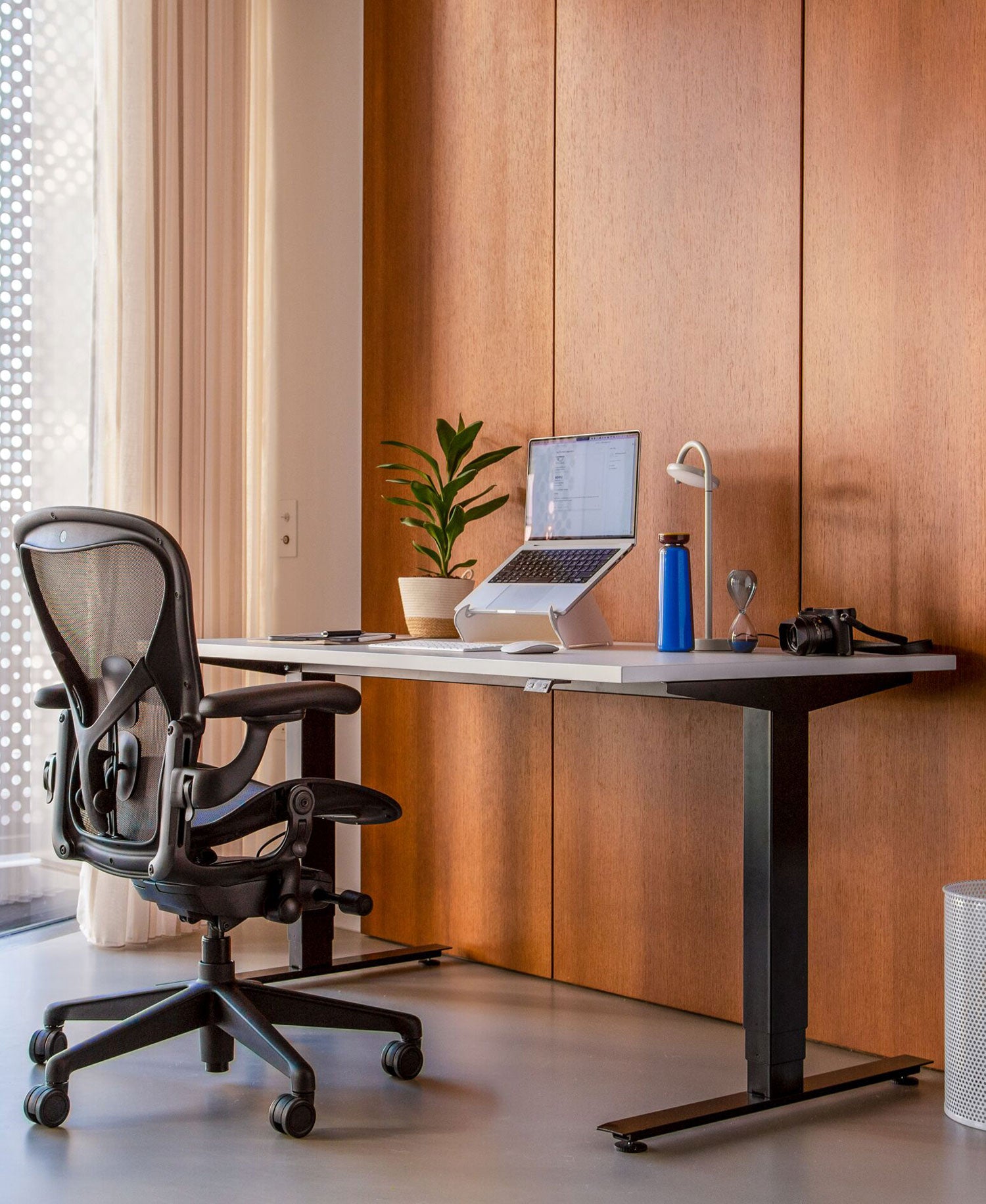 Home-Office mit Aeron-Bürostuhl in Graphit vor Nevi-Sitz-Steh-Schreibtisch mit schwarzen Beinen und weißer Platte und Oripura-Laptop-Ständer.