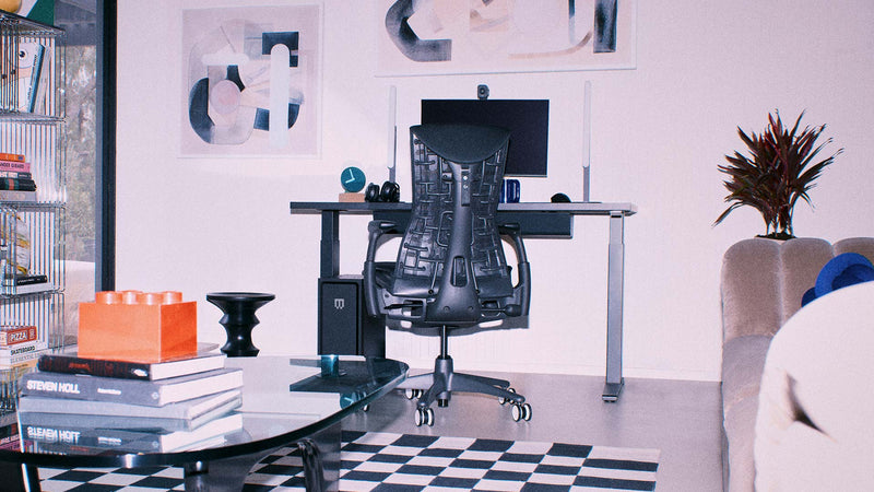 Ein schwarzer ergonomischer Gaming-Stuhl von Herman Miller Embody als Teil einer PC-Gaming-Ausstattung mit einem Nevi-Steh-Sitz-Schreibtisch in einem hellen Wohnbereich.