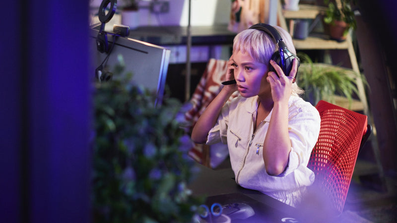 Ein Video einer Frau, die in einem rot-schwarzen Sayl-Gaming-Stuhl von Herman Miller sitzt, Kopfhörer aufsetzt und ein Computerspiel spielt.