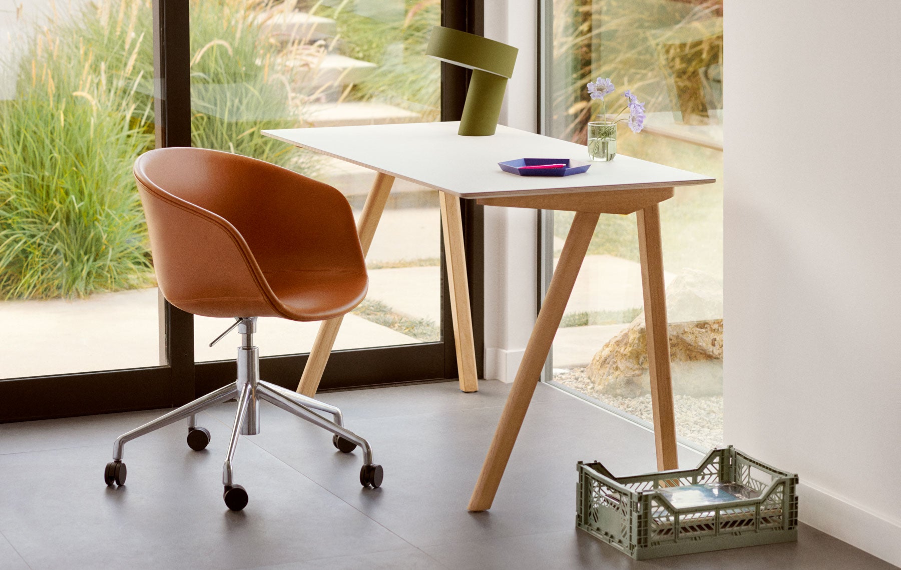 Einfaches Foto in Wohnumgebung mit Blick auf den Garten mit Hay Copenhague 90-Schreibtisch in Eiche mit weißer Platte, mit Hay Slant-Lampe in Khakigrün auf der Platte und kleiner Hay-Aufbewahrungskiste auf dem Boden
