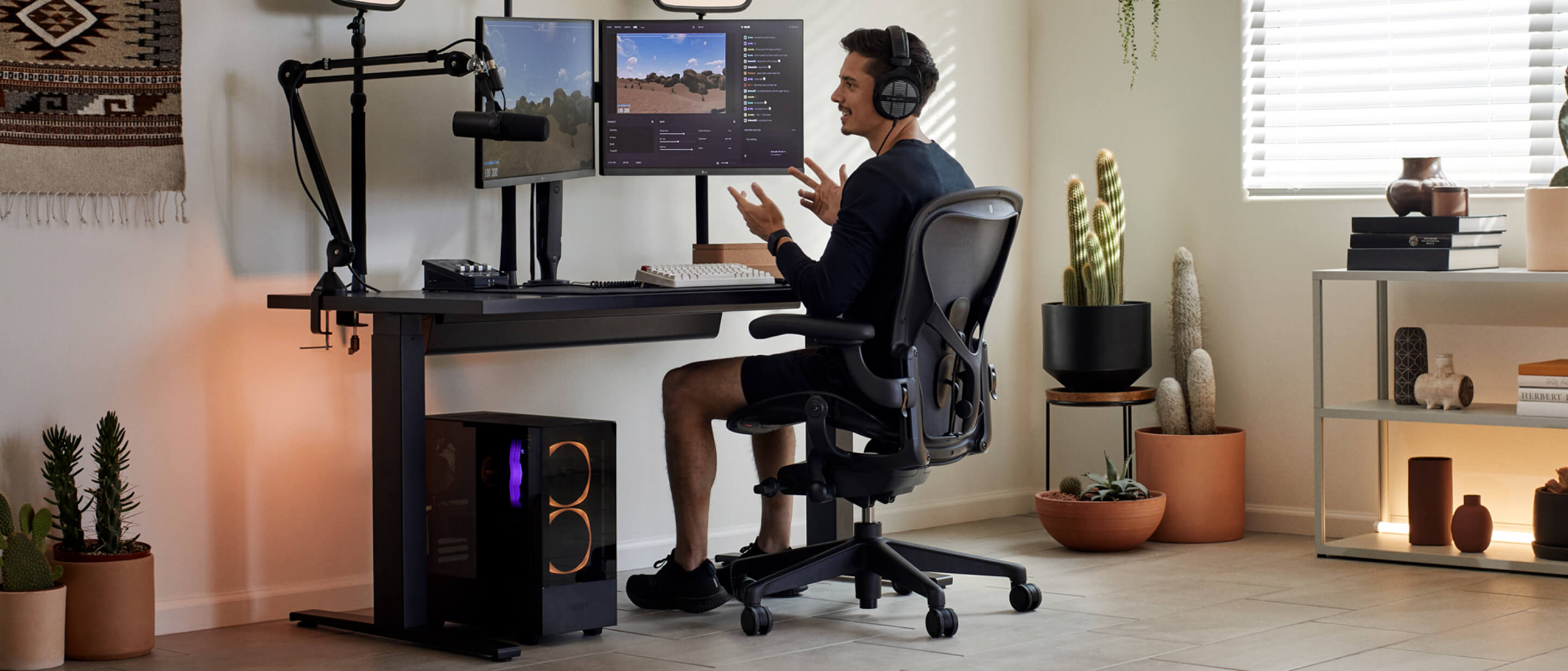 Gamer Xaryu mit erhobenen Händen beim Spielen an seinem Herman Miller-Setup in einem Aeron-Gaming-Stuhl mit Nevi-Gaming-Tisch und Ollin-Dual-Monitorarmen
