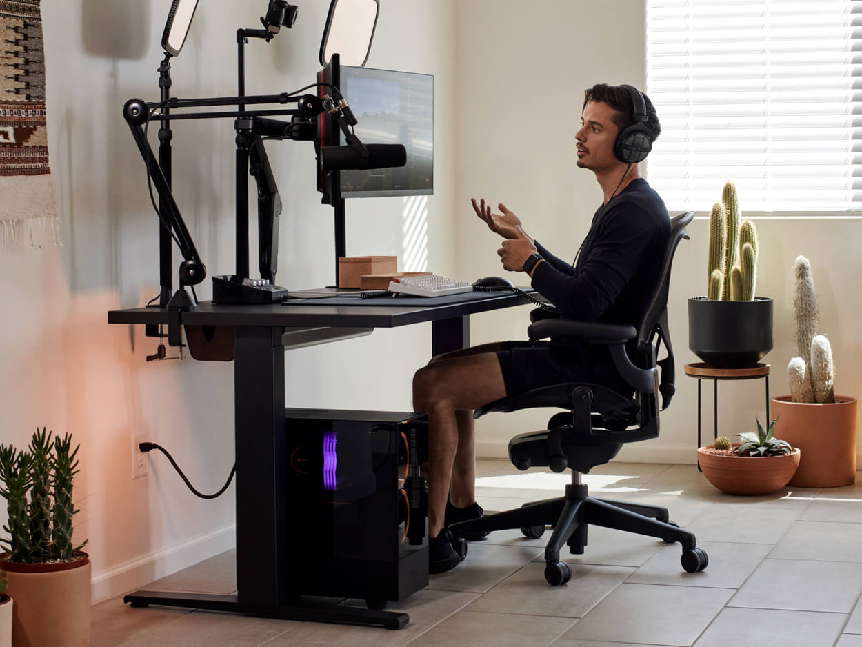 Gamer Xaryu sitzt an seinem Gaming-Set mit einem Aeron Gaming-Stuhl in Graphit, einem Nevi Gaming-Schreibtisch und Ollin Dual-Monitorarmen