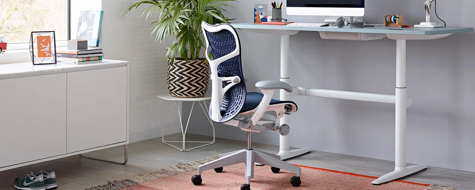 A light home office environment featuring a Twilight Butterfly Back Mirra 2 chair with polished base at a Atlas sit stand desk with a white polygon table in the corner.