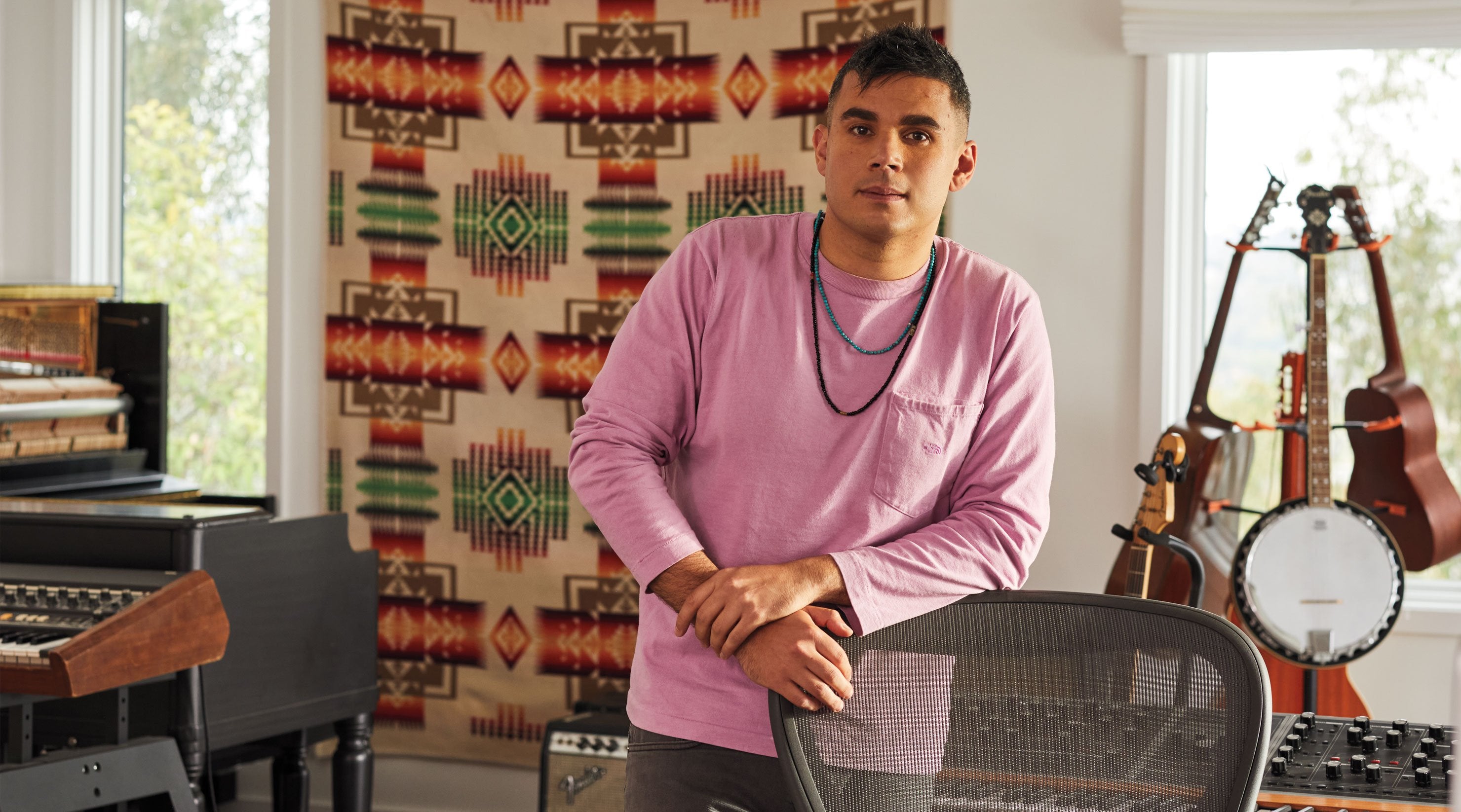 Foto von Rostam, Musiker, Produzent und Komponist, stehend an einen Aeron-Bürostuhl in Graphit gelehnt, mit Musikinstrumenten im Hintergrund